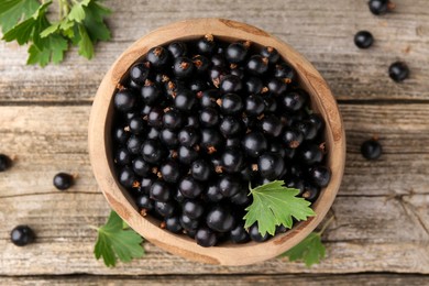 Ripe black currants and leaves in bowl on wooden table, top view