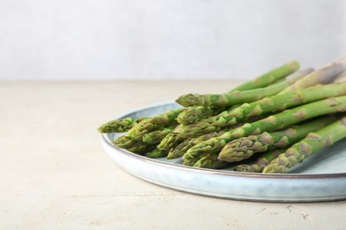 Photo of Plate with fresh green asparagus stems on light textured table, closeup. Space for text