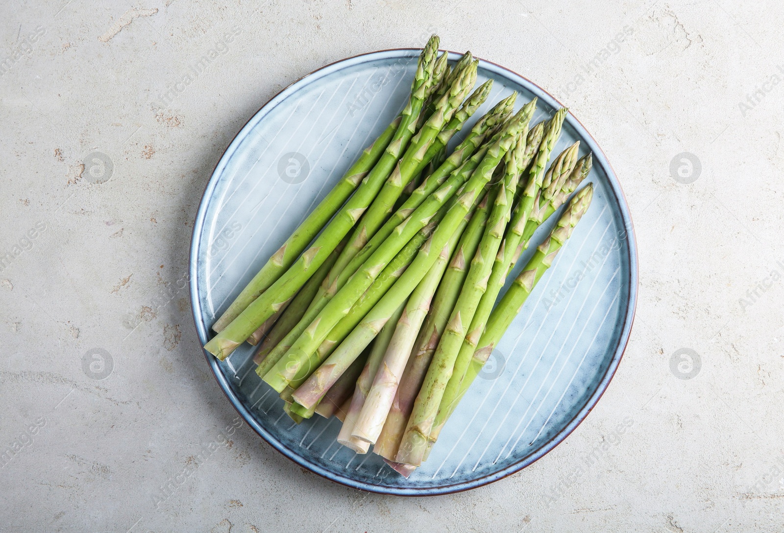 Photo of Plate with fresh green asparagus stems on light textured table, top view