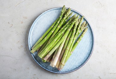 Photo of Plate with fresh green asparagus stems on light textured table, top view