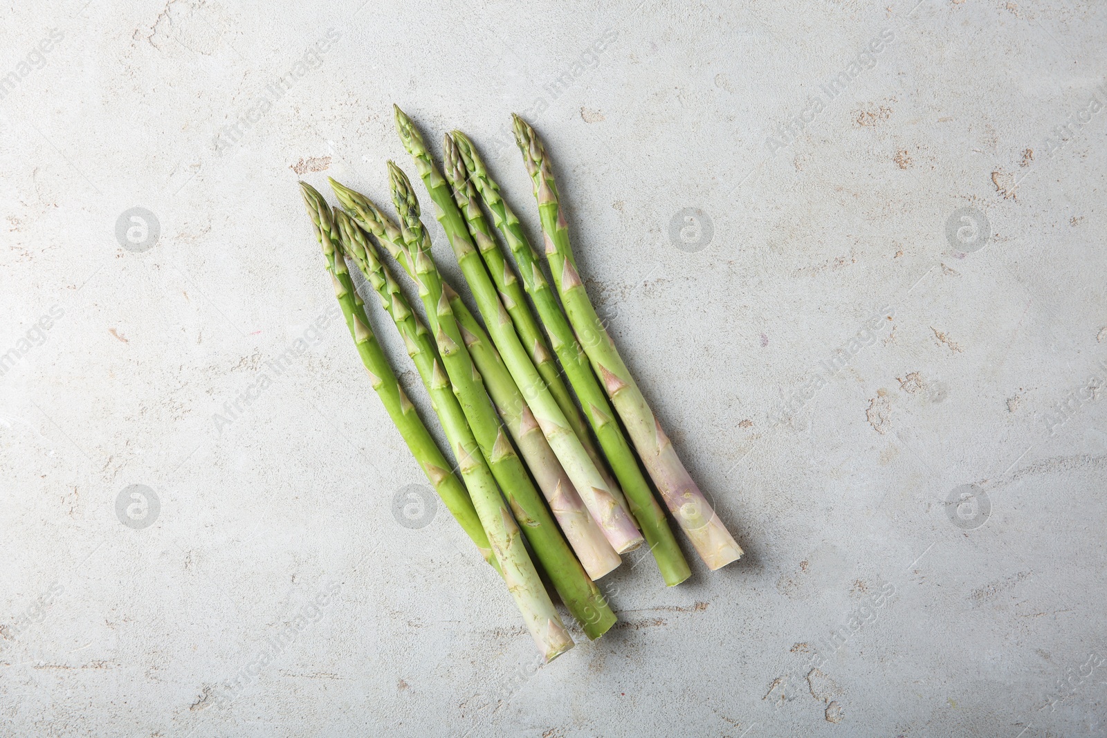 Photo of Many fresh green asparagus stems on light textured table, top view