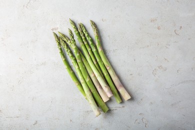 Photo of Many fresh green asparagus stems on light textured table, top view