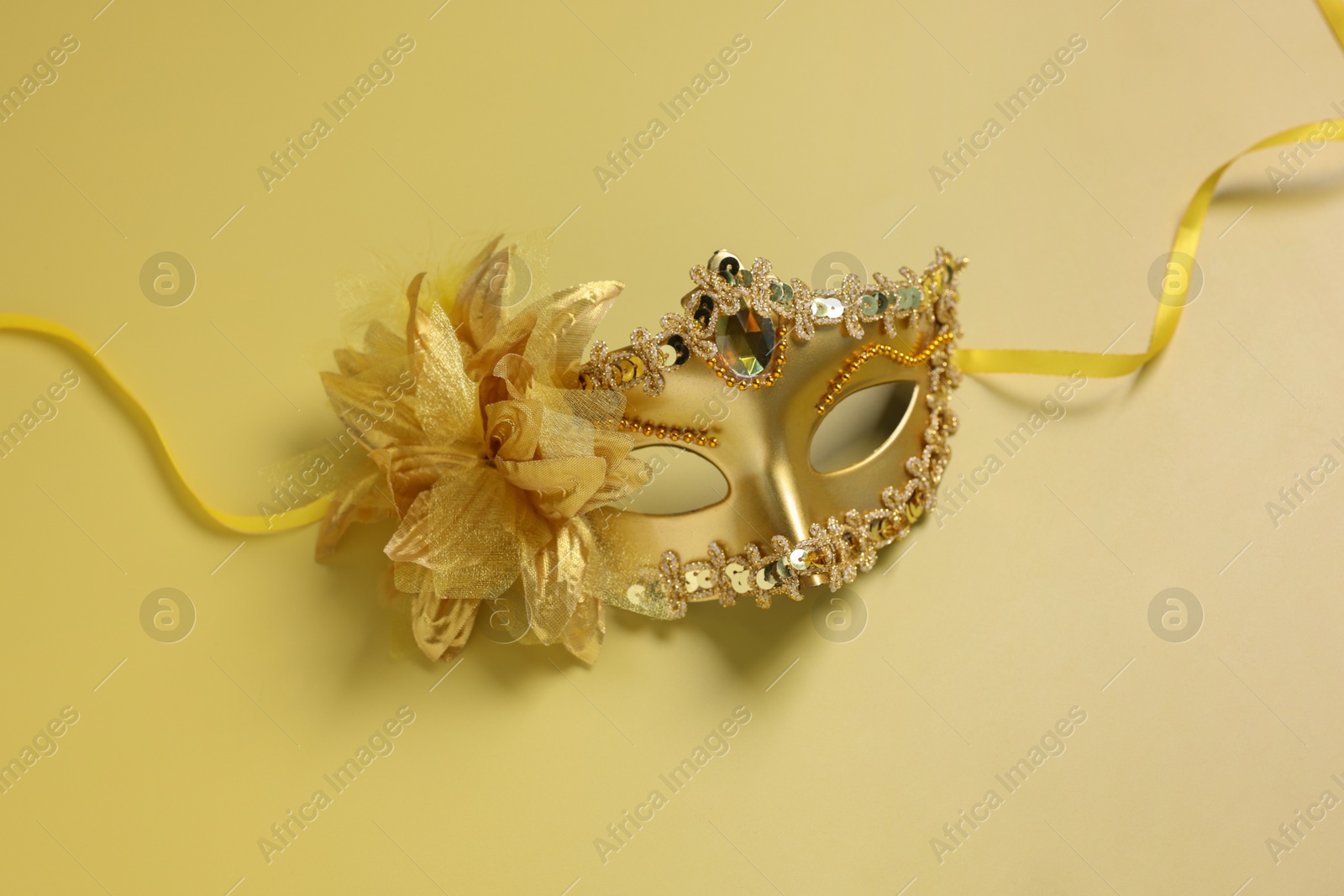 Photo of Beautiful carnival mask on yellow background, top view