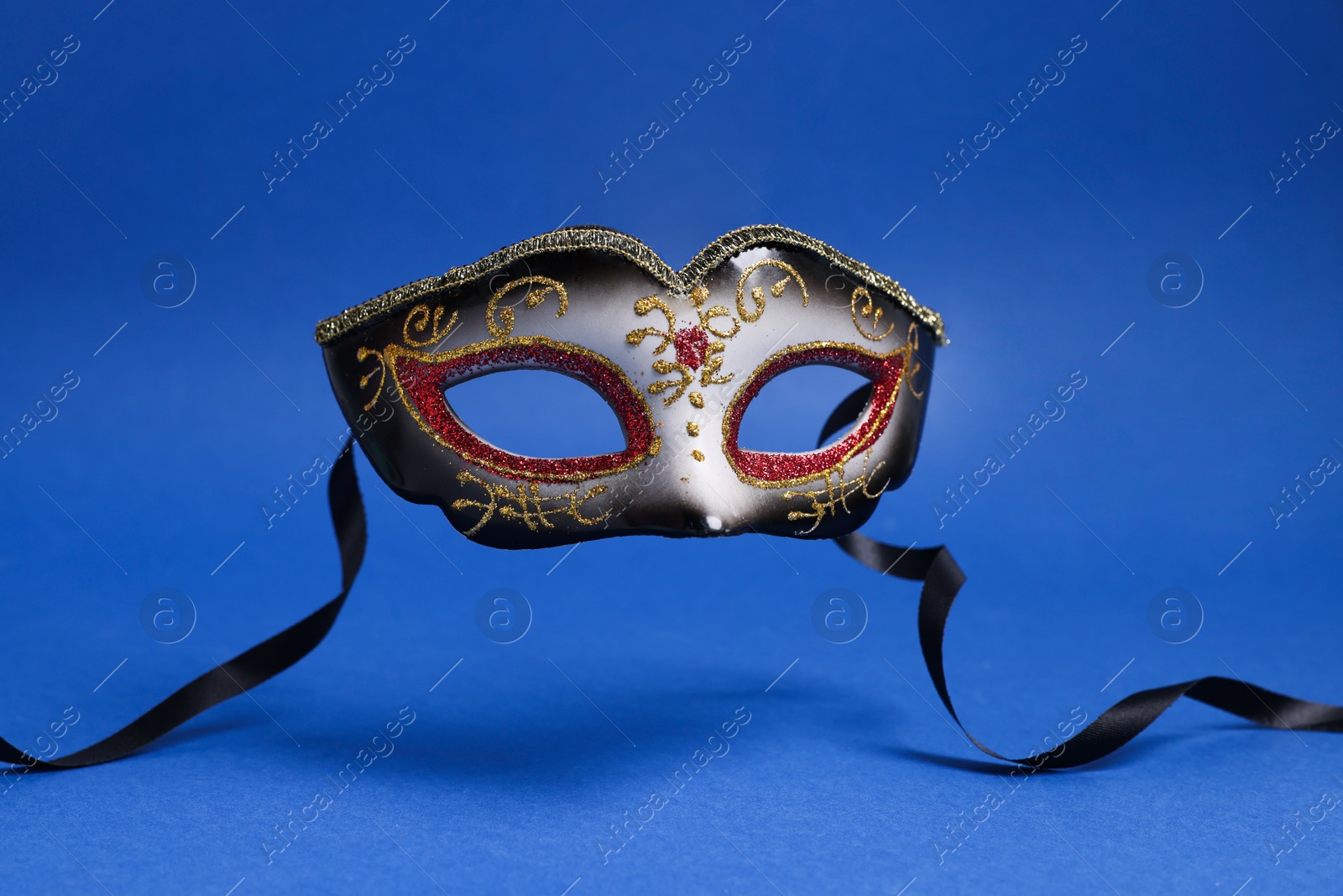 Photo of Beautiful carnival mask in air on blue background