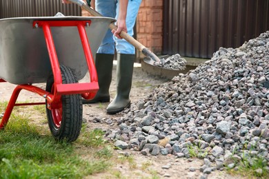 Photo of Man with shovel full of stones and wheelbarrow outdoors, closeup