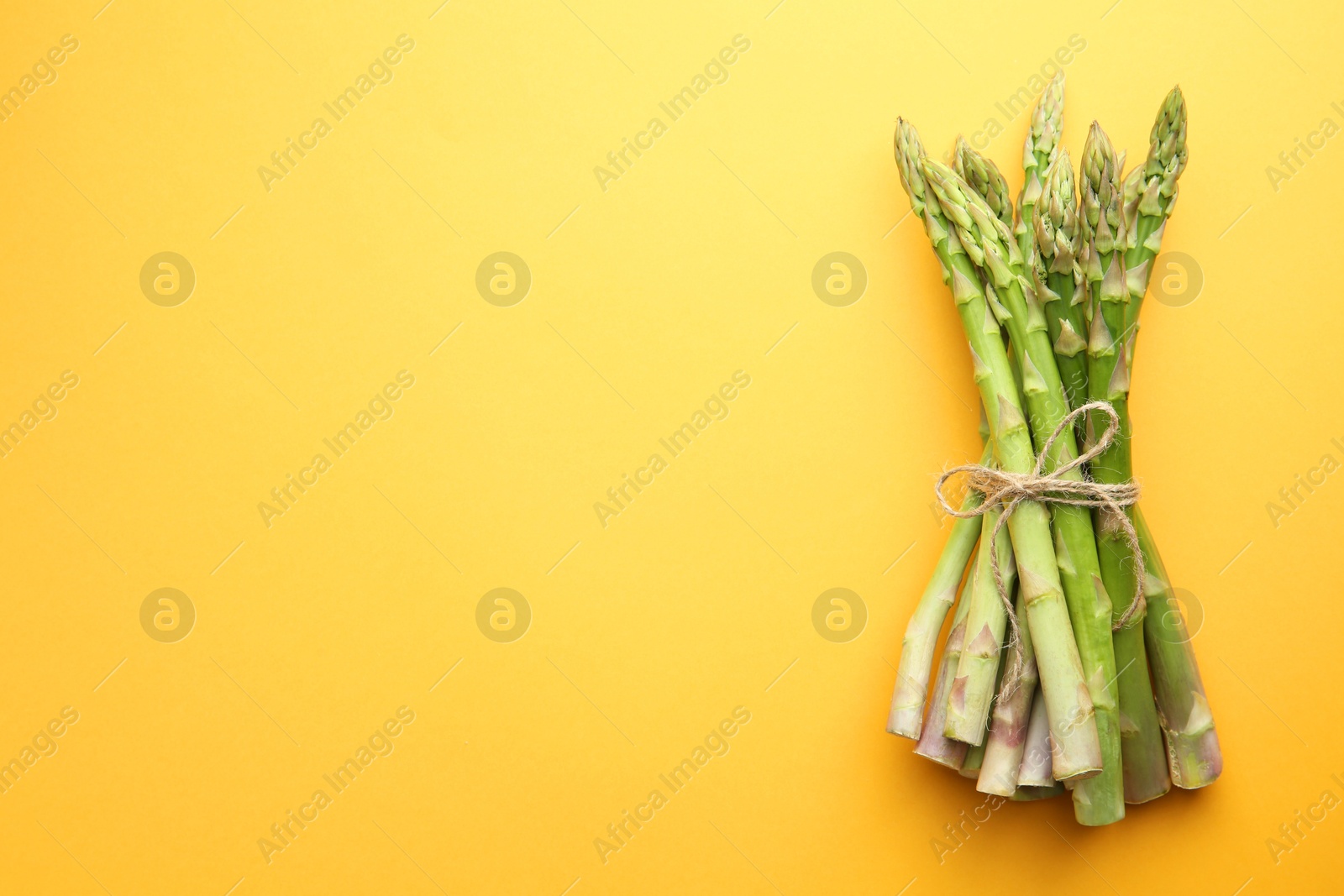 Photo of Fresh green asparagus stems on orange table, top view. Space for text