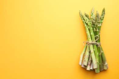 Fresh green asparagus stems on orange table, top view. Space for text