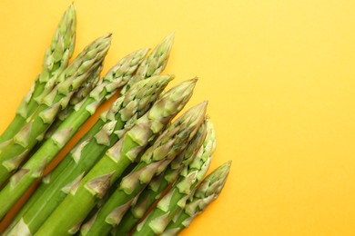 Photo of Fresh green asparagus stems on orange table, top view. Space for text