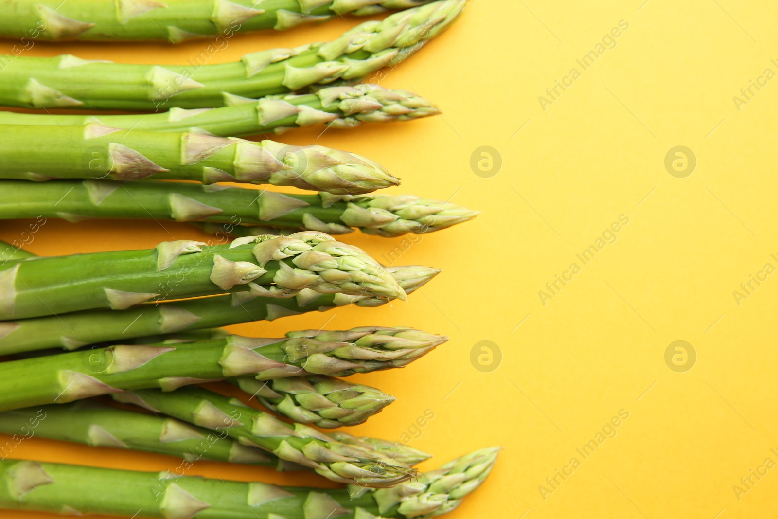 Photo of Fresh green asparagus stems on orange table, top view. Space for text