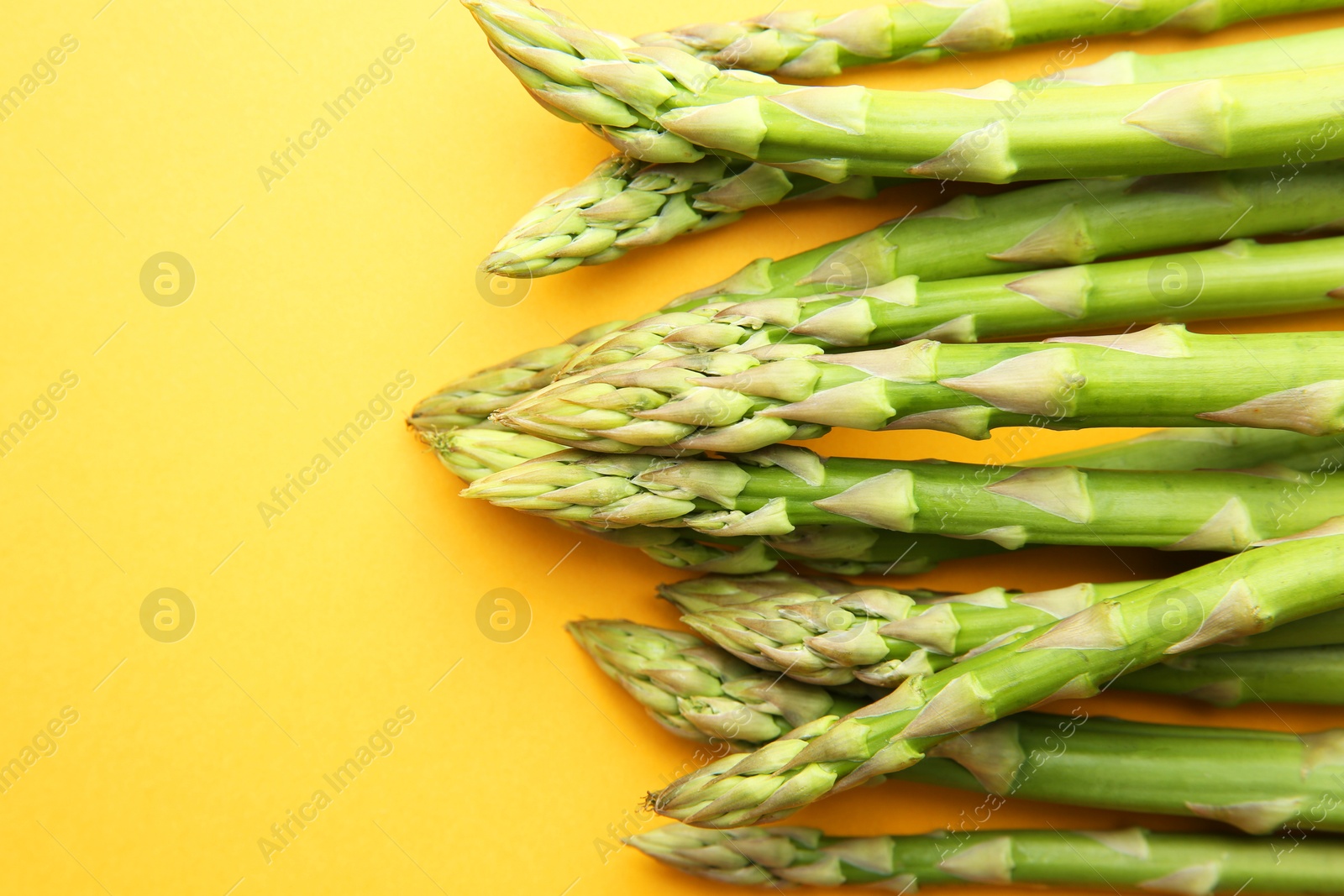 Photo of Fresh green asparagus stems on orange table, top view. Space for text