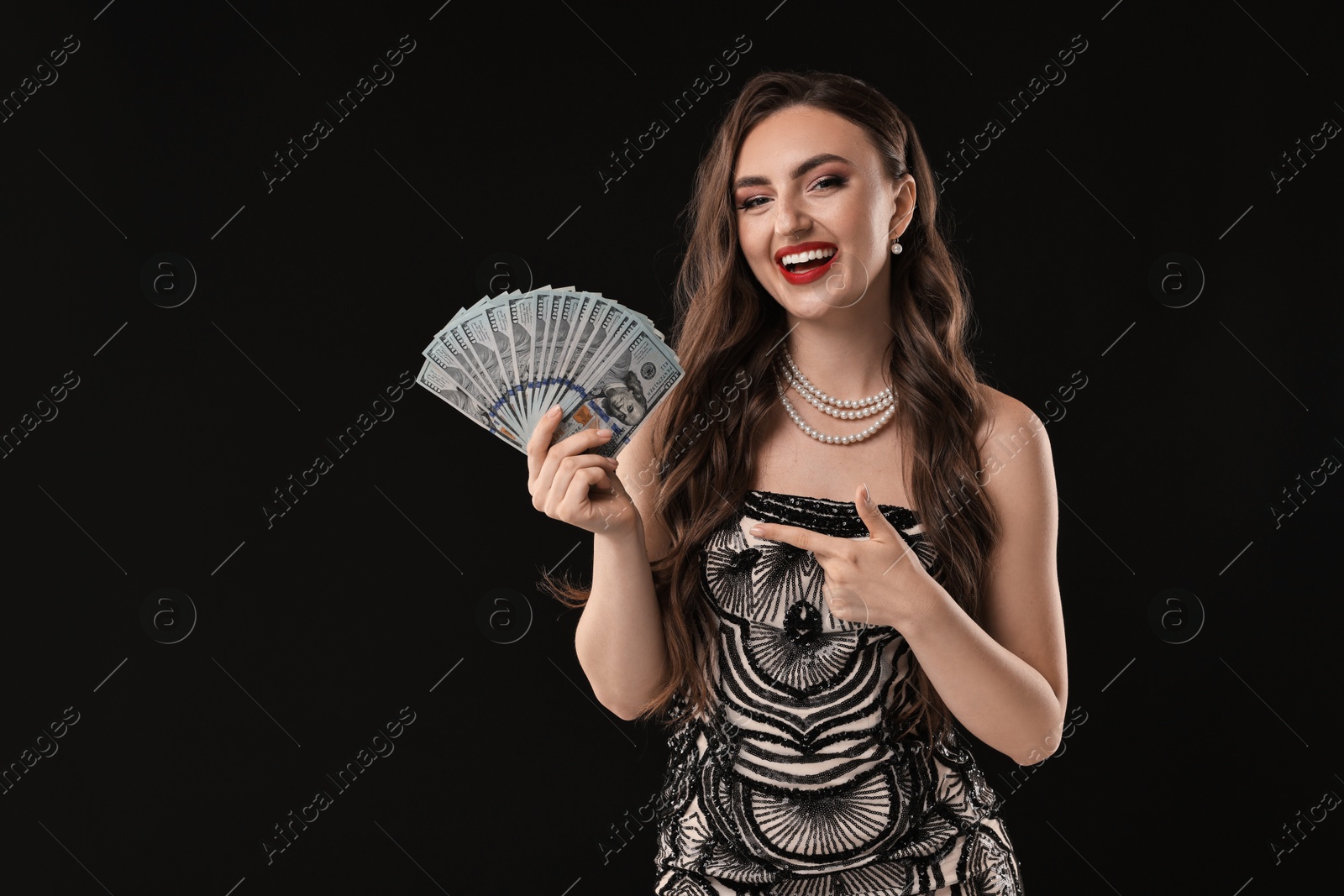 Photo of Smiling woman pointing at dollar banknotes on black background. Space for text