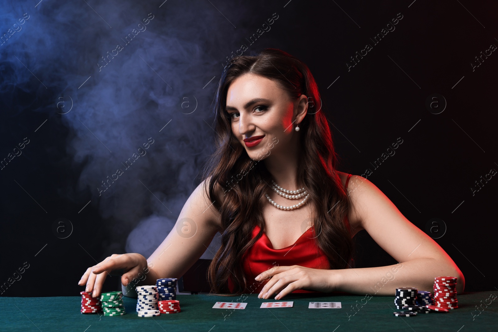 Photo of Charming woman playing poker at table on black background with smoke