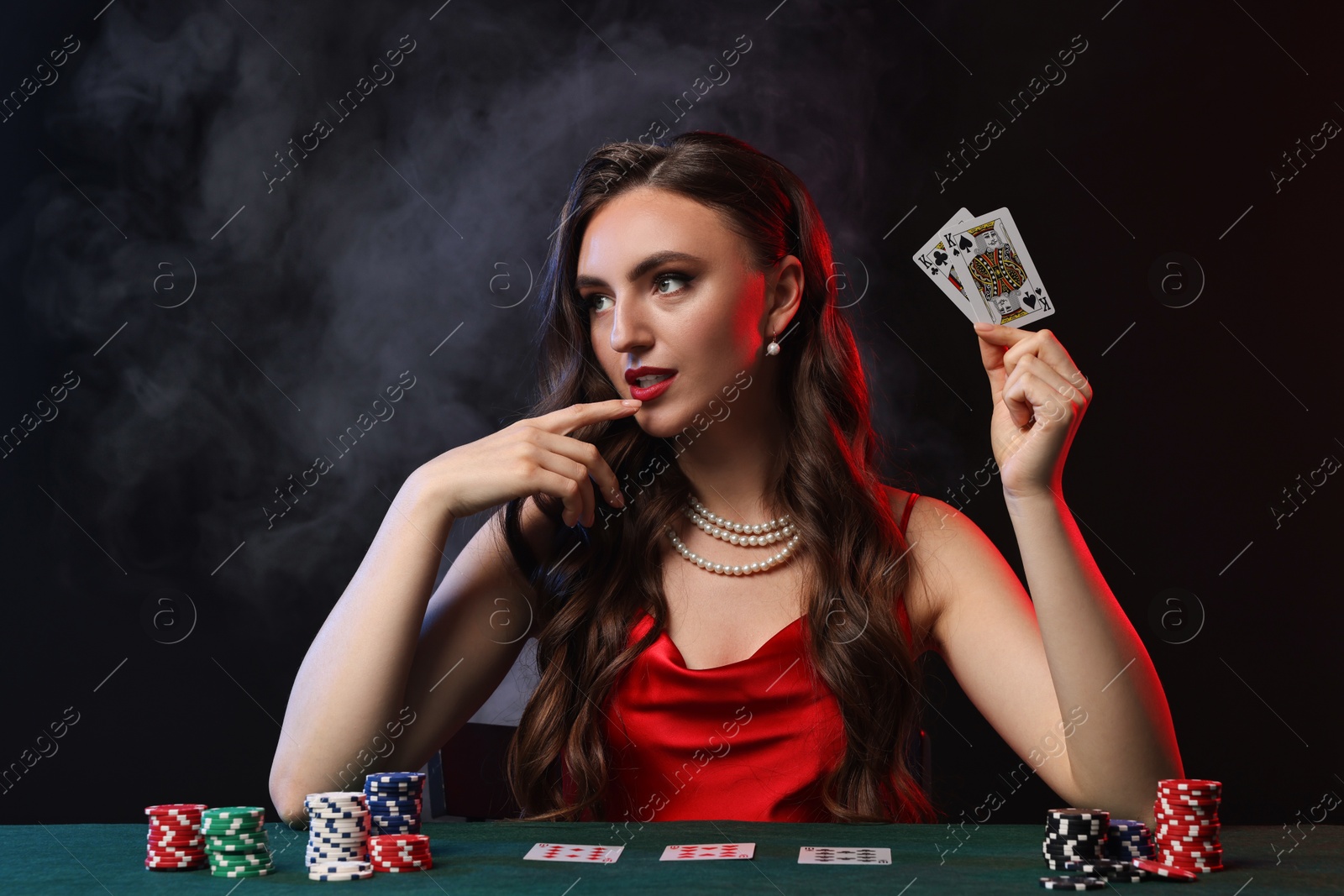 Photo of Charming woman playing poker at table on black background with smoke