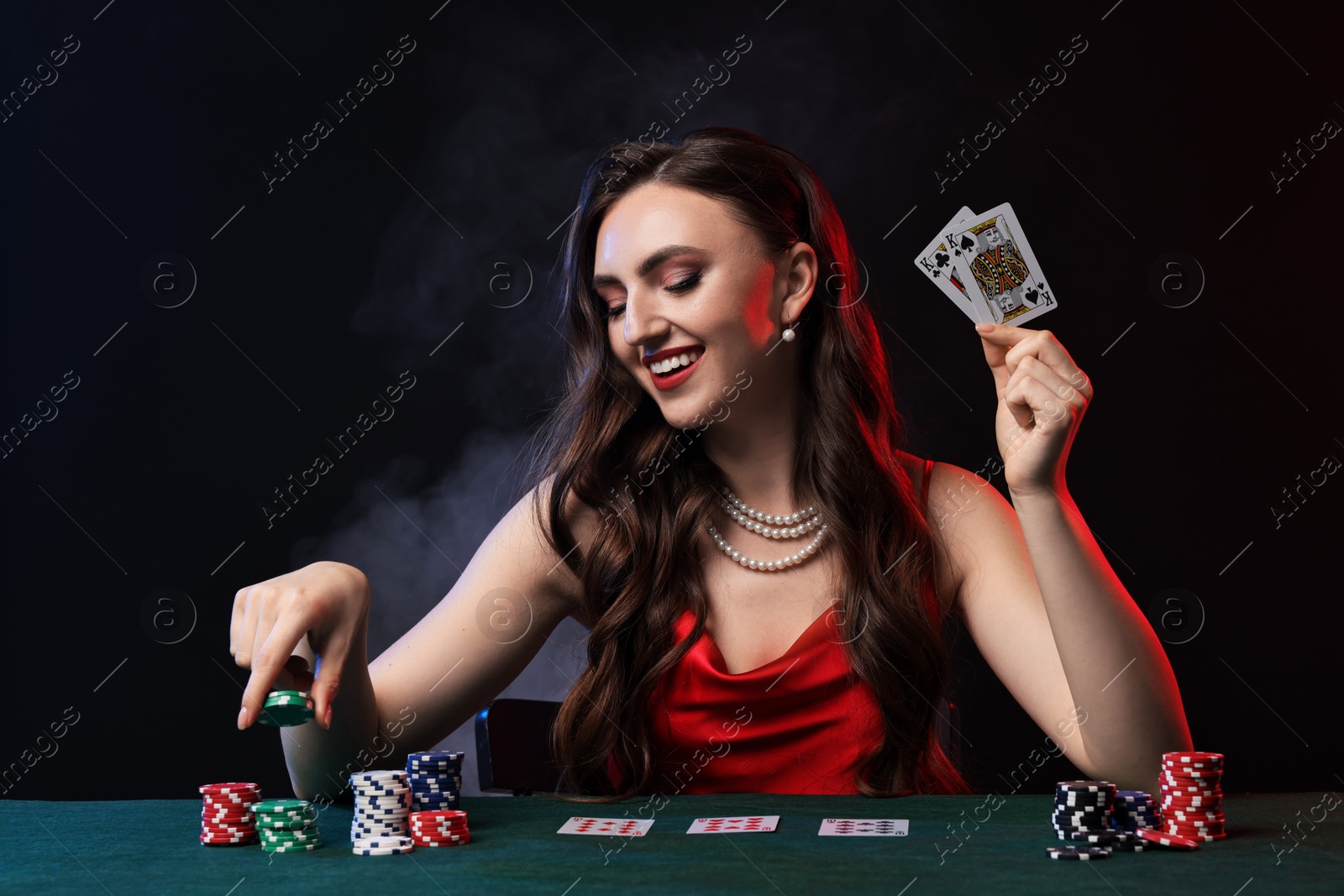 Photo of Smiling woman playing poker at table on black background with smoke