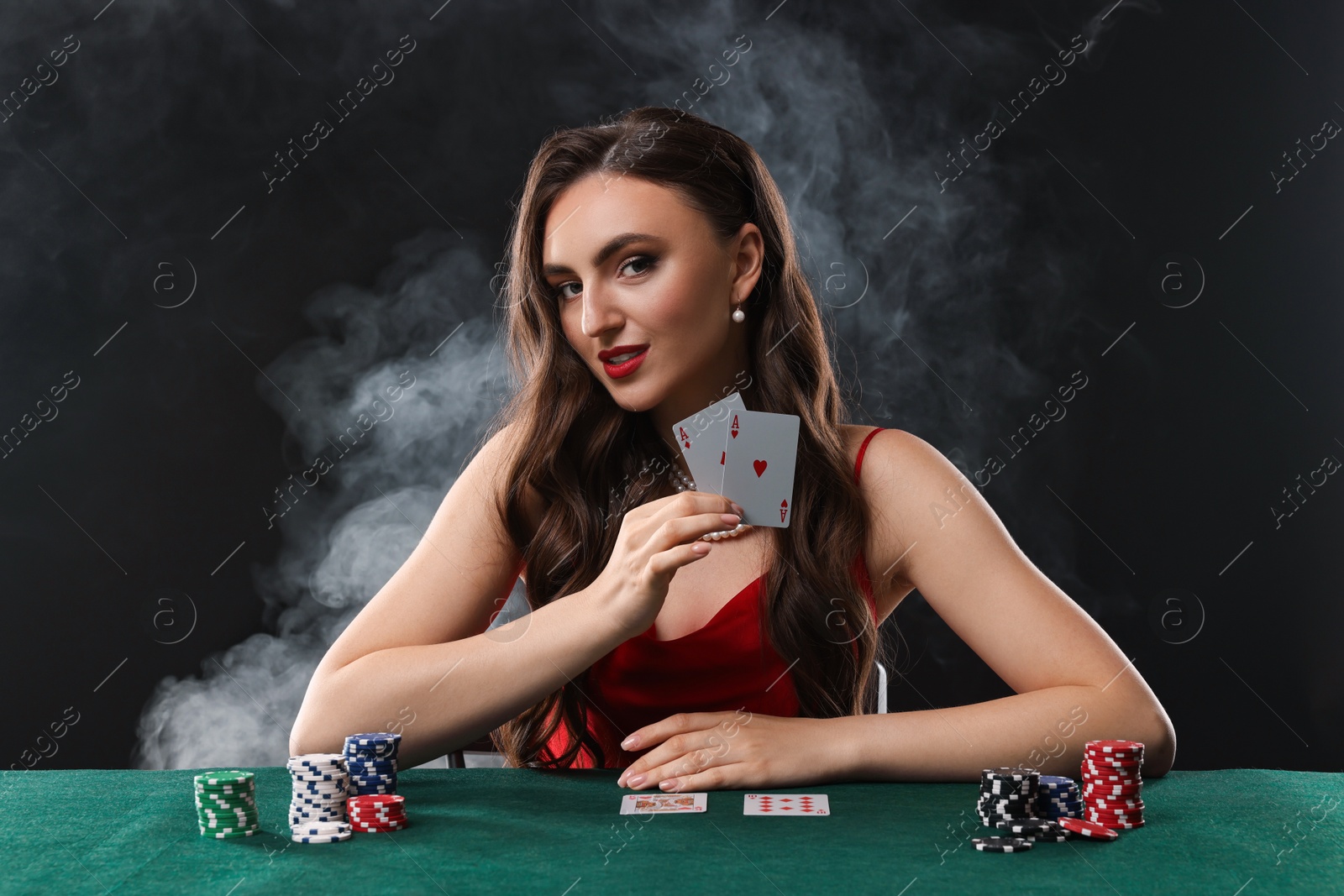 Photo of Charming woman playing poker at table on black background with smoke