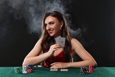 Photo of Smiling woman playing poker at table on black background with smoke