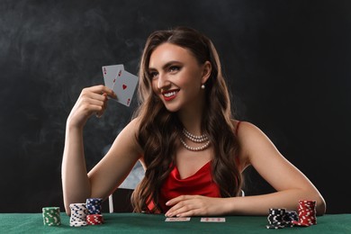 Smiling woman playing poker at table on black background with smoke