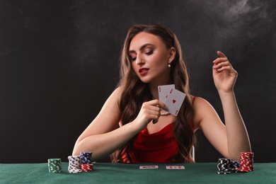 Photo of Charming woman playing poker at table on black background with smoke