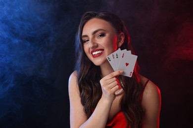 Poker game. Smiling woman with playing cards on black background in color lights and smoke