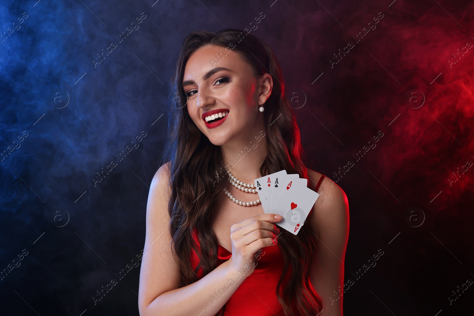 Photo of Poker game. Smiling woman with playing cards on black background in color lights and smoke