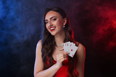 Poker game. Smiling woman with playing cards on black background in color lights and smoke