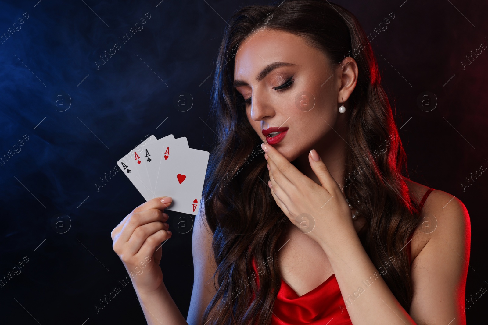 Photo of Poker game. Charming woman with playing cards on black background in color lights and smoke