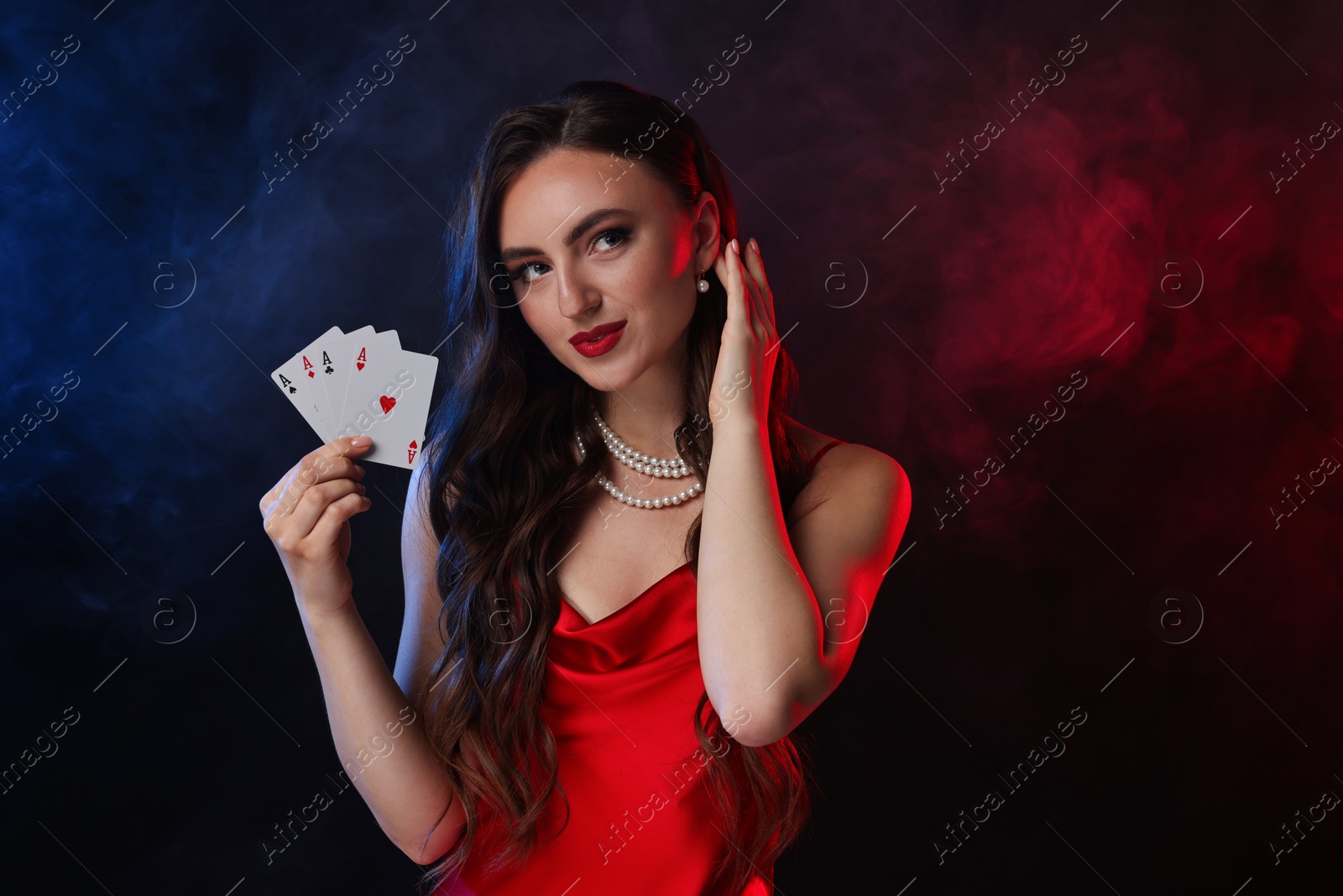 Photo of Poker game. Charming woman with playing cards on black background in color lights and smoke