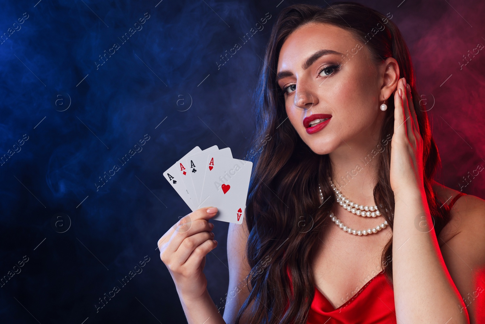 Photo of Poker game. Charming woman with playing cards on black background in color lights and smoke. Space for text