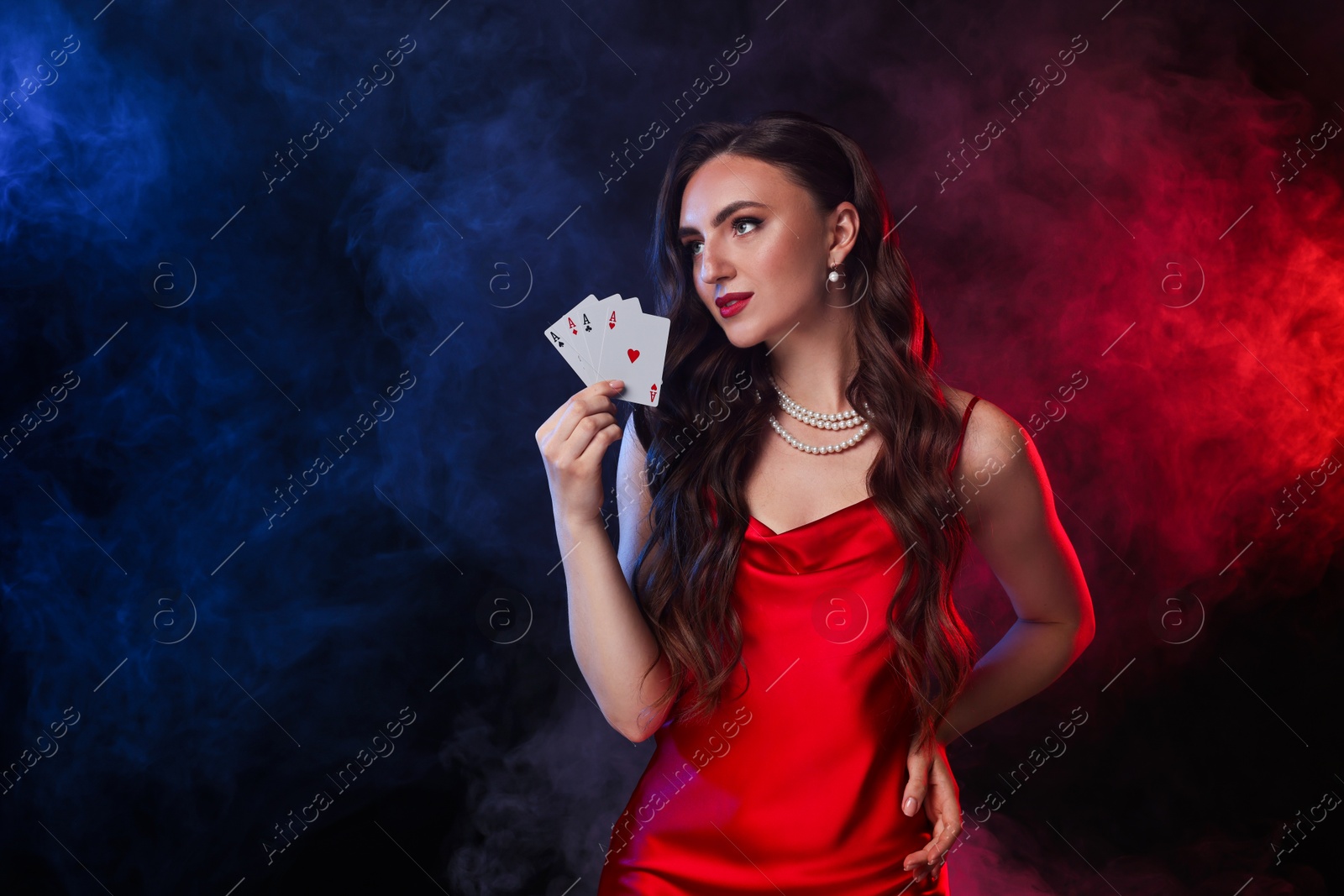 Photo of Poker game. Charming woman with playing cards on black background in color lights and smoke. Space for text