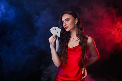 Poker game. Charming woman with playing cards on black background in color lights and smoke. Space for text