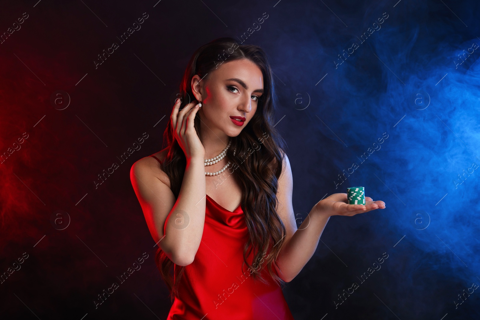 Photo of Charming woman with poker chips on black background in color lights and smoke