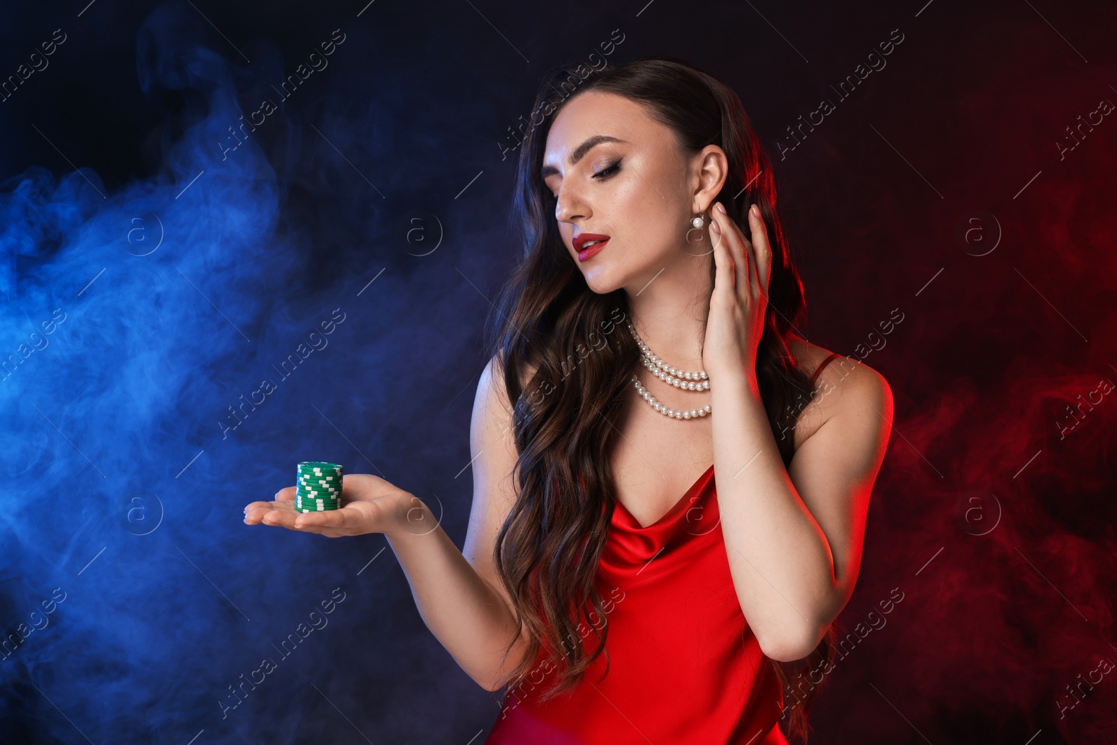 Photo of Charming woman with poker chips on black background in color lights and smoke