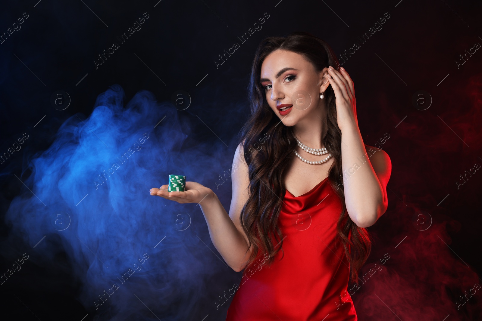 Photo of Charming woman with poker chips on black background in color lights and smoke. Space for text