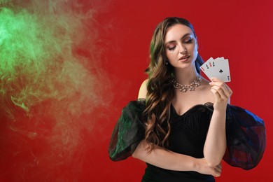 Poker game. Charming woman with playing cards on red background in color lights and smoke. Space for text