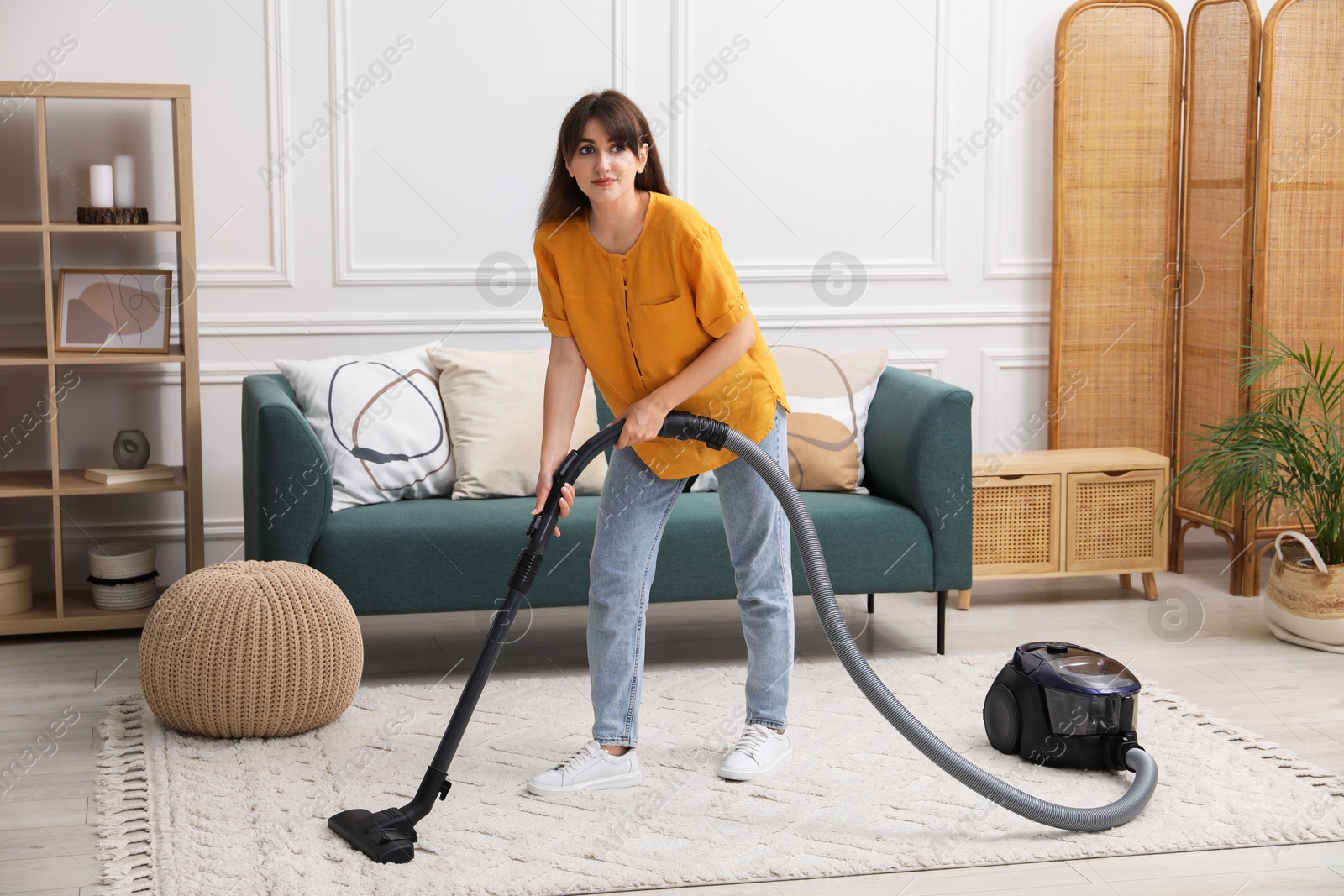 Photo of Young woman cleaning carpet with vacuum in living room