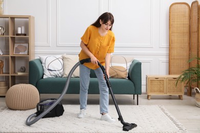 Photo of Young woman cleaning carpet with vacuum in living room