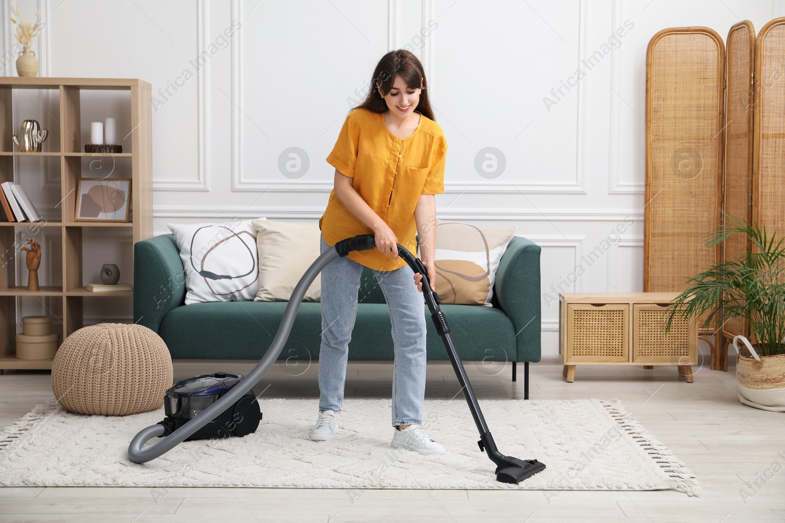 Photo of Young woman cleaning carpet with vacuum in living room