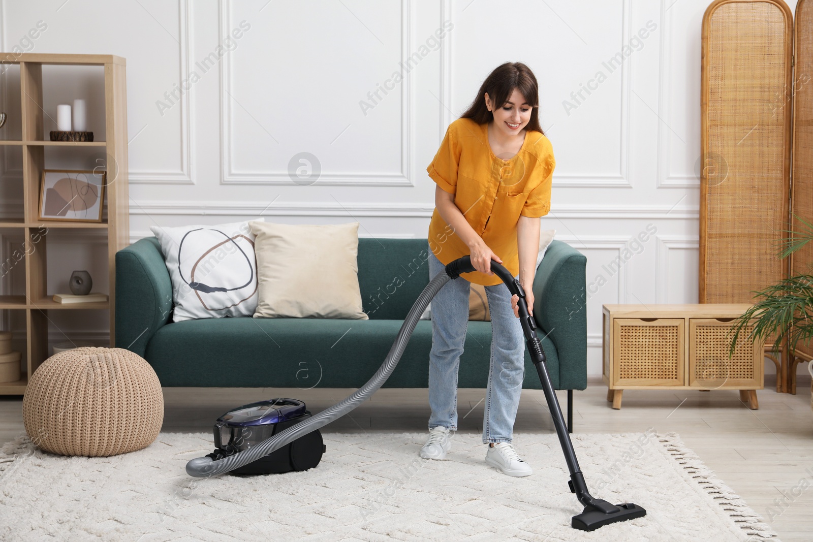 Photo of Young woman cleaning carpet with vacuum in living room