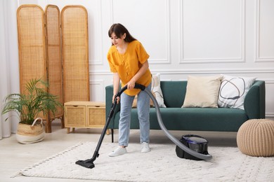 Photo of Young woman cleaning carpet with vacuum in living room