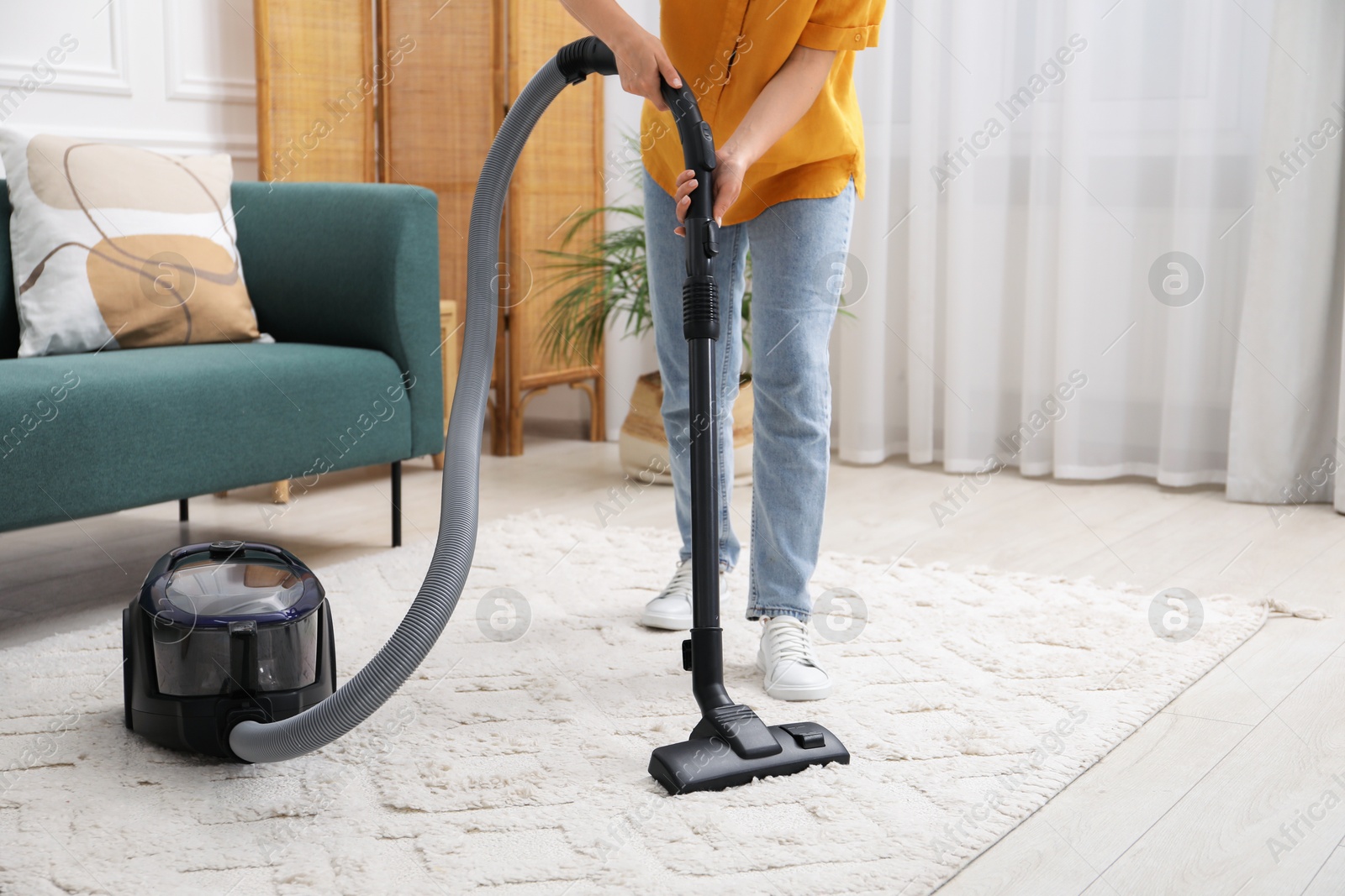 Photo of Woman cleaning carpet with vacuum in living room, closeup