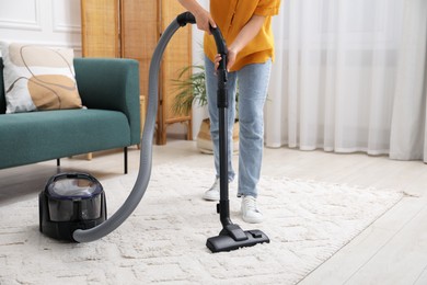 Woman cleaning carpet with vacuum in living room, closeup