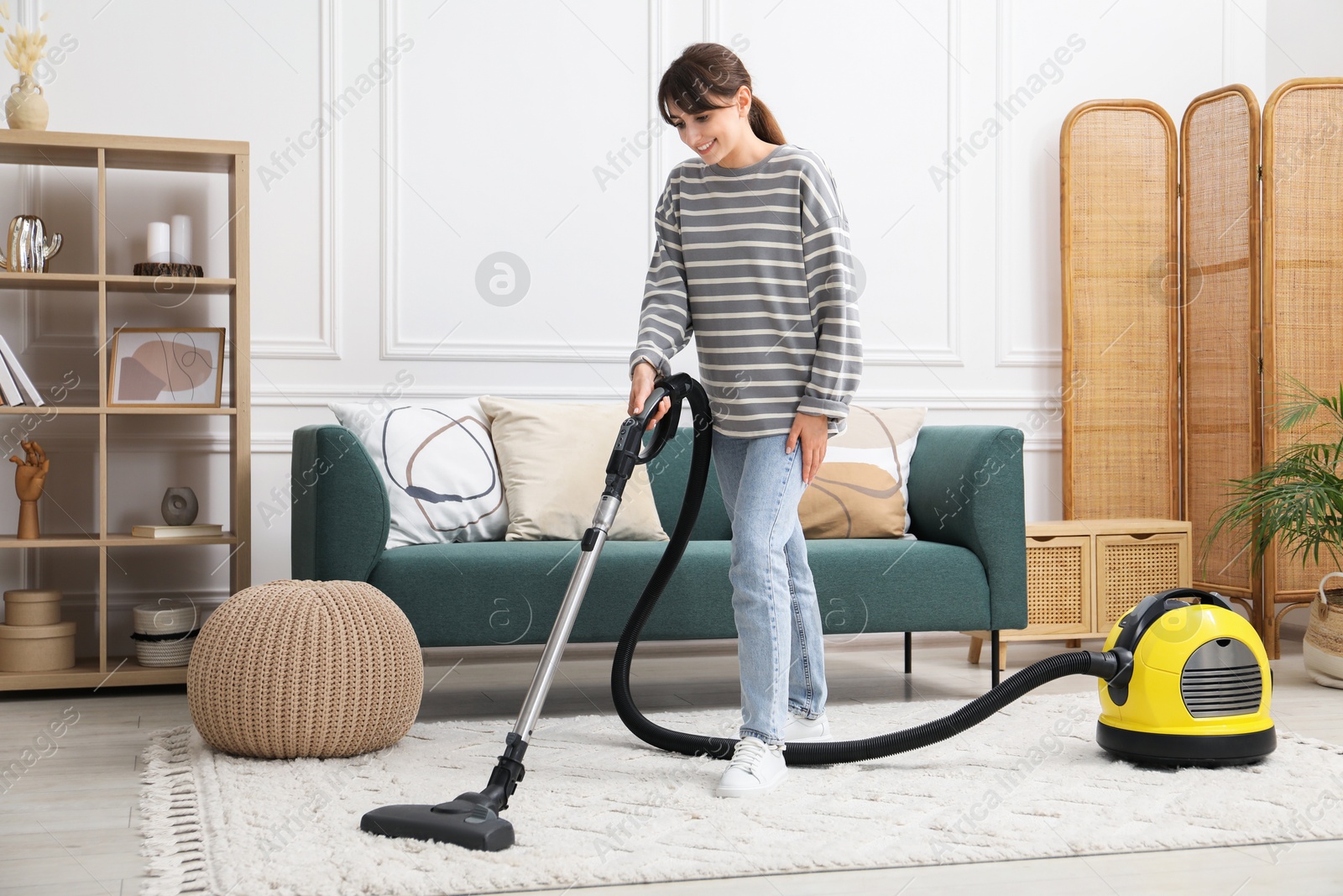 Photo of Young woman cleaning carpet with vacuum in living room