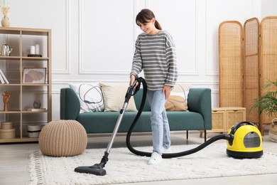 Young woman cleaning carpet with vacuum in living room