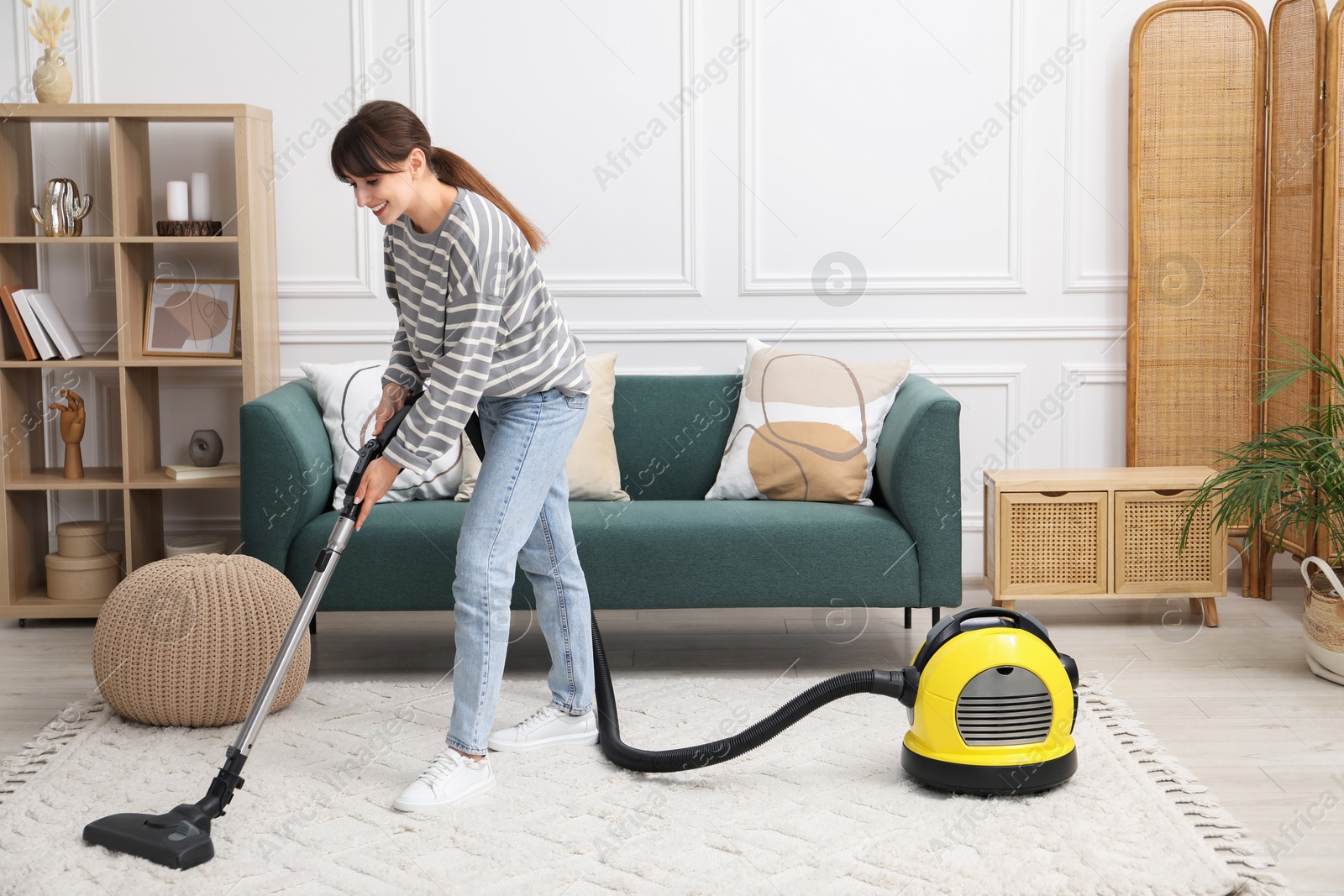 Photo of Young woman cleaning carpet with vacuum in living room