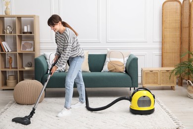 Photo of Young woman cleaning carpet with vacuum in living room