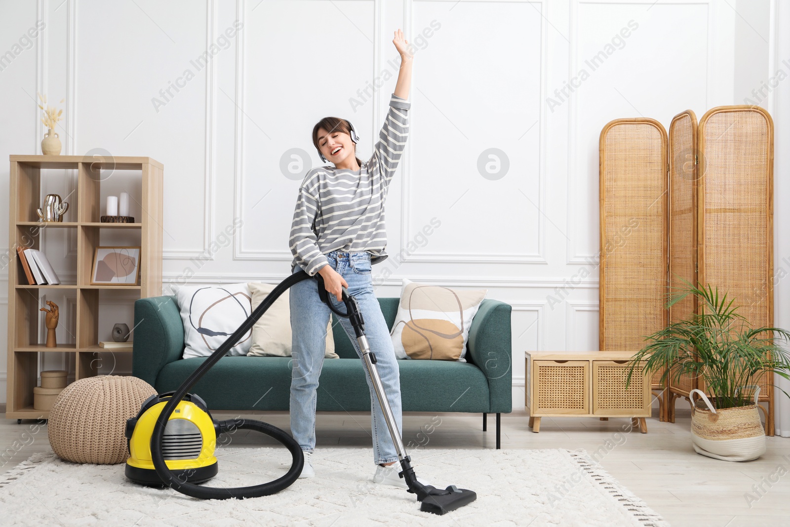 Photo of Young woman in headphones having fun while cleaning carpet with vacuum in living room