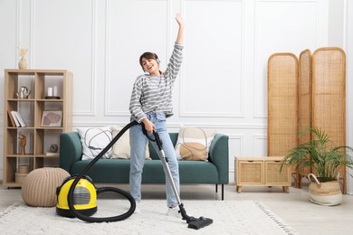 Photo of Young woman in headphones having fun while cleaning carpet with vacuum in living room