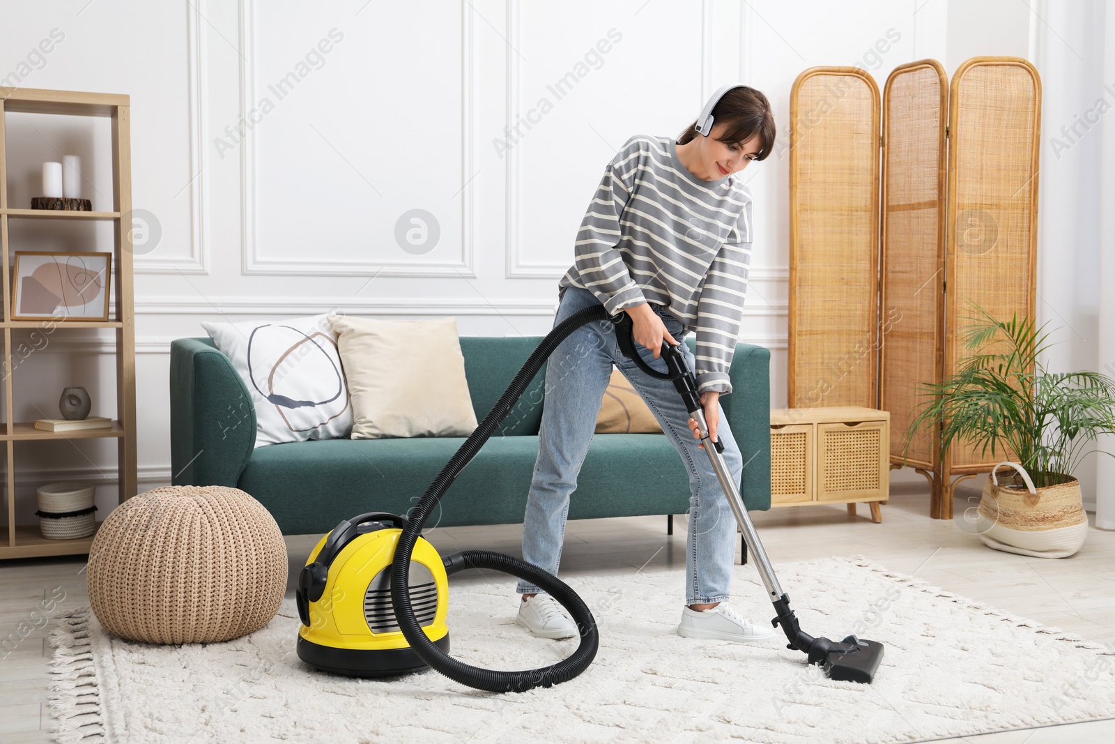 Photo of Young woman wearing headphones cleaning carpet with vacuum in living room