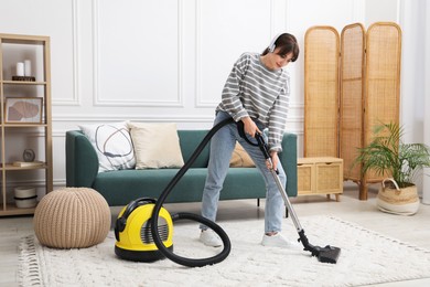 Young woman wearing headphones cleaning carpet with vacuum in living room