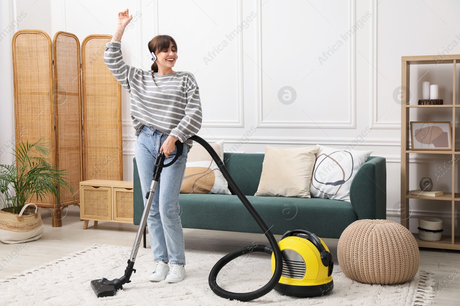 Photo of Young woman wearing headphones cleaning carpet with vacuum in living room